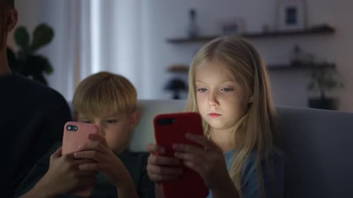 Children Using Mobile Phones with Parent on Sofa