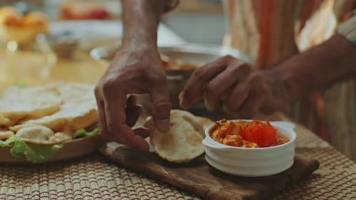 Adding Fresh Coriander to Indian Dish Served with Flatbread on Wooden Board