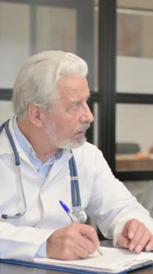 Senior Doctor Taking Notes at Desk in Office