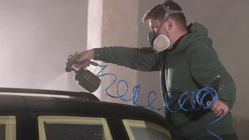 Man Painting Car with Spray Gun in Garage