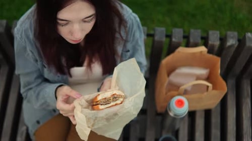 Young Woman Eats Burger on Park Bench