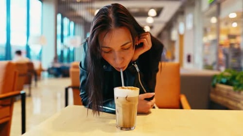 In a Modern Cafe a Young Woman Sits Enjoying Iced Coffee Wearing a Chic Leather Jacket Exuding a