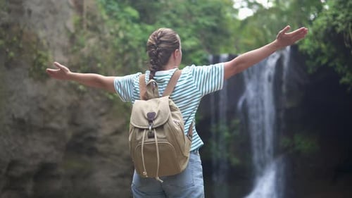 Female tourist with backpack is enjoying view of a waterfall