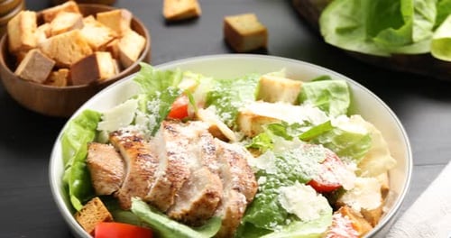 Leckerer Caesar-Salat, serviert auf einem schwarzen Holztisch, Nahaufnahme. Kamera bewegt sich nach rechts