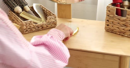 Woman chooses hairbrush at dressing table in home