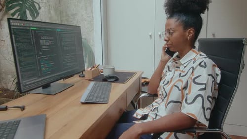 Female IT Specialist Watching Computer Code and Talking on Phone