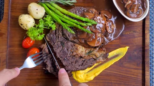 Steak with Mushrooms Being Cut on Wooden Platter