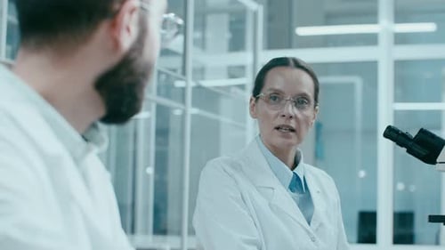 Scientists Discussing Research at Microscope in Laboratory