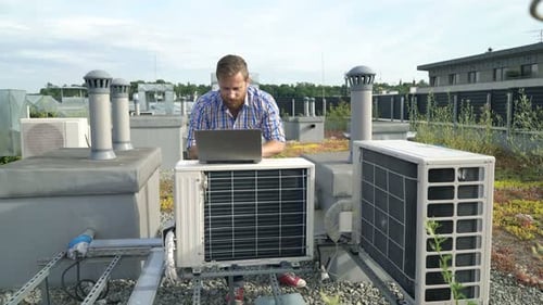 HVAC Technician Using Laptop on Urban Rooftop