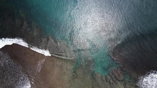 Zumbido aéreo de olas rompiendo en el océano que muestra el arrecife debajo, que tiene grietas y
