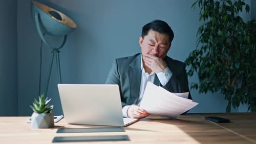 Sleepy Office Worker Sitting at Desk with Laptop and Documents During Work Day