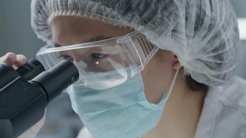 Wissenschaftler für Schutzmasken und Schutzbrillen unter Verwendung des Mikroskops im Labor