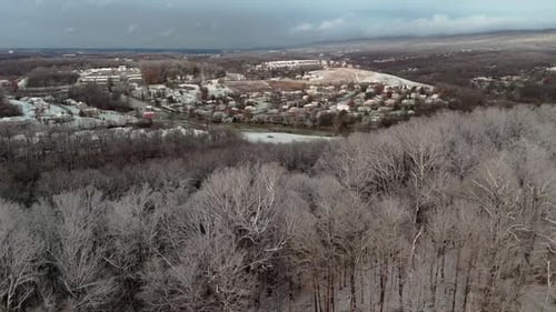 Aerial Winter Ascend Over Forest to Suburb Surrounded by Snow-Covered Hills