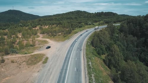 Luftaufnahme eines Intercity-Highways mit Verkehr, der an einem strahlend sonnigen Tag durch einen grünen Wald fließt