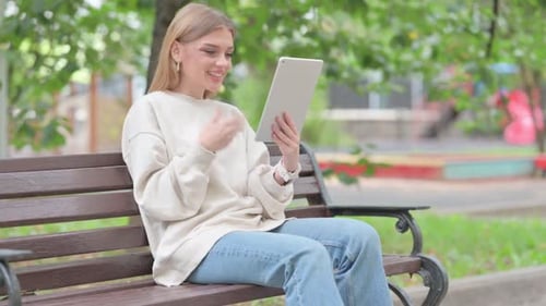 Young Woman Doing Video Chat on Tablet while Sitting Outdoor on a Bench