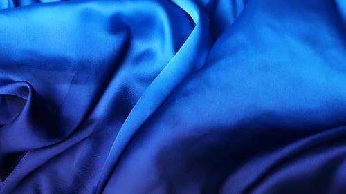 Natürlicher blauer Seidenstoff, der im Wind flattert. Abstrakte fließende Wellen erzeugen einen bewegten Hintergrund.