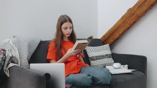 Young Girl Reads a Book While Sitting Comfortably on a Sofa in a Cozy Living Room Setting with