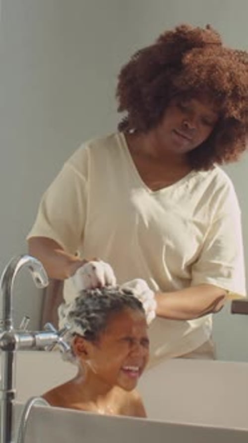 Woman washing child's hair in bathtub at home