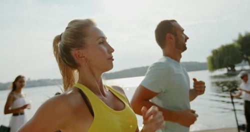 Athletic Adults Running on Sunny Riverfront Path