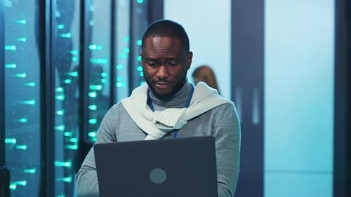 A Focused Man Works on a Laptop in a Hightech Server Room