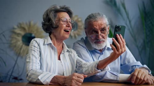 Senior Couple Laughing Looking at Smartphone Indoors