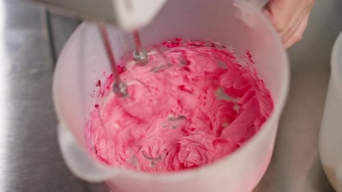 Primer plano de una panadera en una cocina profesional mezclando crema y tinte con una batidora