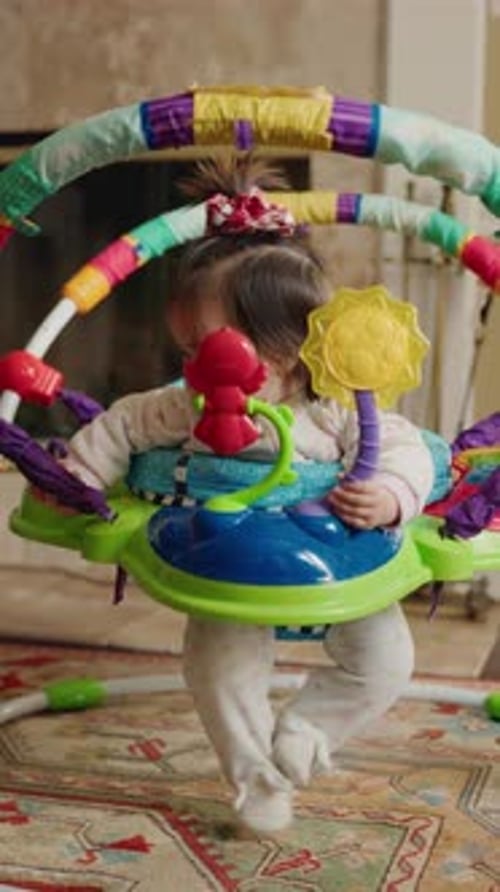Petite fille debout et rebondissant dans un pull d'activités coloré tenant des jouets lumineux et les explorant
