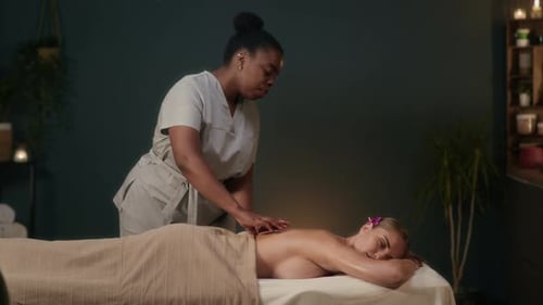Young Masseuse Performing Relaxing Body Massage on Female Client in Spa Parlor