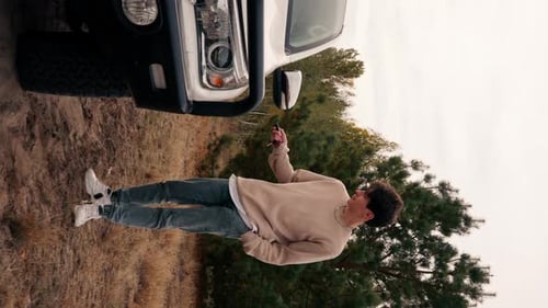 Successful young guy disarms his new car for trip traveling along the road in the forest alone