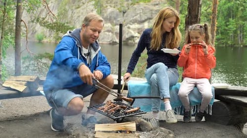 A Couple with a Child Grilling in the Forest on the Shore of the Lake