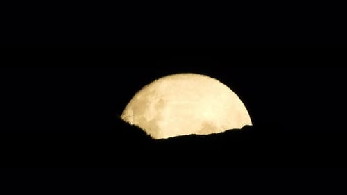Haunted full moon rising slowly above mountain edge with rocks and plant detail, ominous and scary