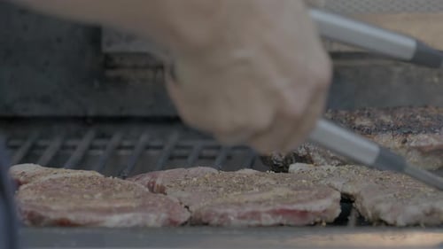 Closeup of steaks being placed on a hot grill outside.