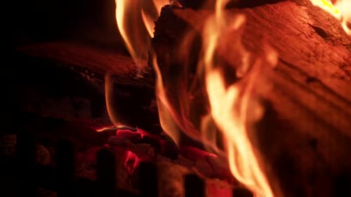 Glowing hot flames on side of wooden log in fireplace, orange heat