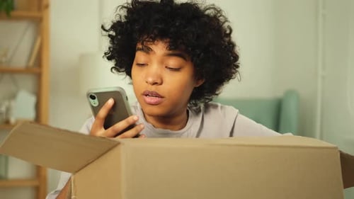 Young Woman Using Phone by Open Cardboard Box