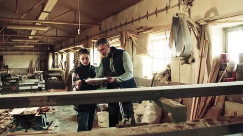 Man And Woman Workers In The Carpentry Workshop Holding Wood.