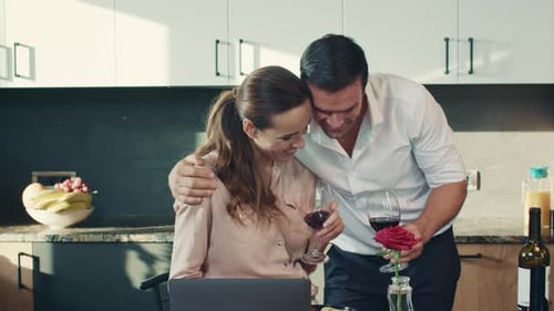 Couple enjoying wine in kitchen looking at laptop