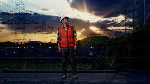 Close Up Back View Of Asian Male Engineer Talking On Smartphone Near High voltage tower