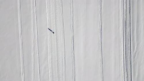 A runner who is running on a snow covered frozen lake on a cold sunny winter day. Top down drone foo