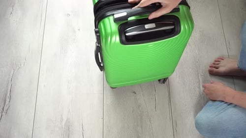 Guy rotate the green baggage case with clothes in hand luggage. Tourist pack things for a trip