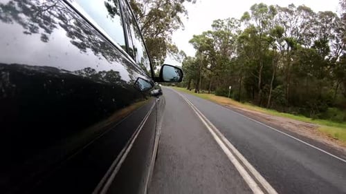 Tracking shot of a car driving down an Australian highway through a forest and meadows.