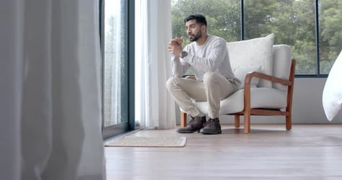 Thoughtful biracial man looking through window at home, slow motion, copy space