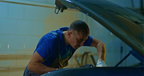 Focused Mechanic Inspecting Car Engine with Spotlight