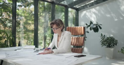 Eine junge Architektin, die mit Bauplänen eines Hauses oder einer Wohnung auf ihrem Schreibtisch arbeitet und Spuren hinterlässt oder