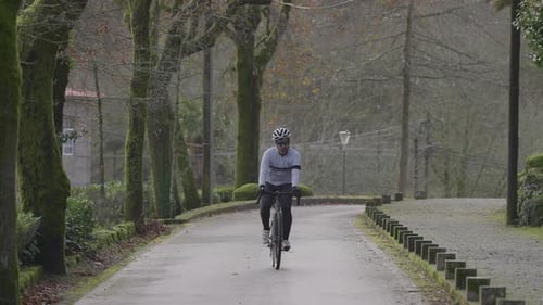Cyclist riding toward camera on park road in slow motion