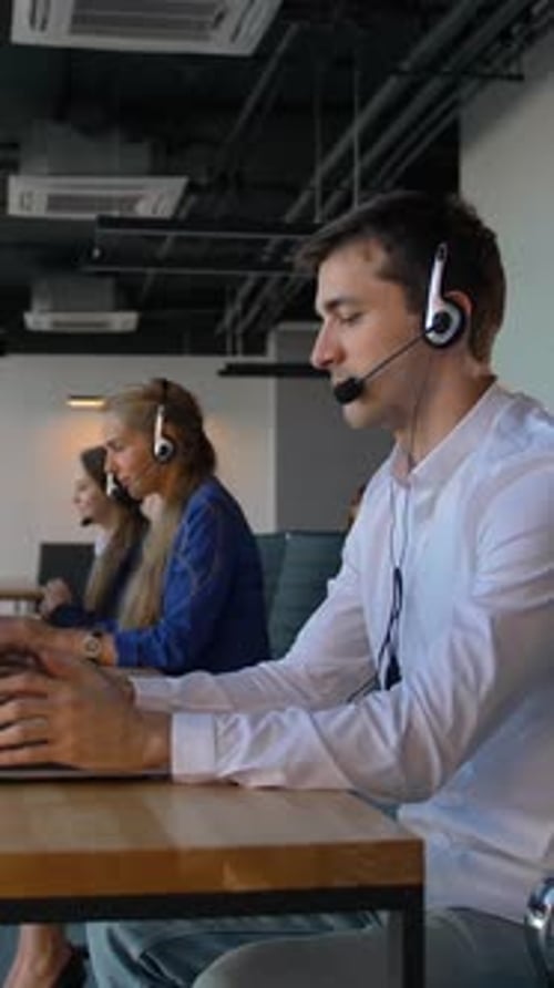 Vertical of Man in Shirt Using a Headset with Laptop While Working in Call Center Office