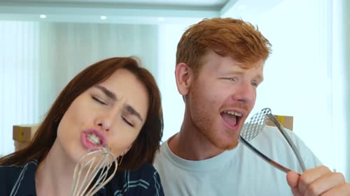 Close Up of Positive Couple Handsome Man and Pretty Woman Singing and Dancing Using Kitchen Utensil