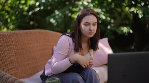 A Young Woman Engaged in a Professional Online Meeting While Relaxing in a Beautiful Garden