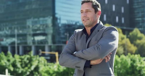 4k video footage of a handsome young businessman posing with his arms folded in the city