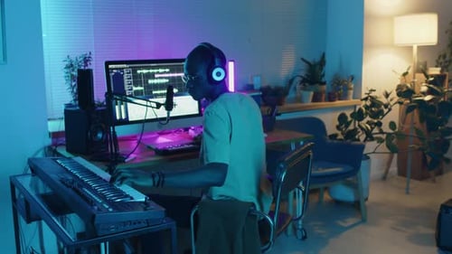 Musician in Headphones Using Synthesizer and Computer at Home Recording Studio