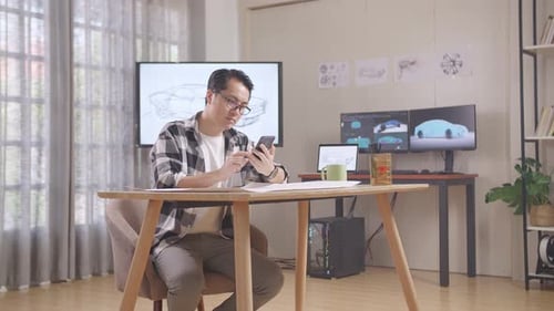 Asian Male Comparing His Design To The Photo On His Smartphone While Working On Car Design Sketch
